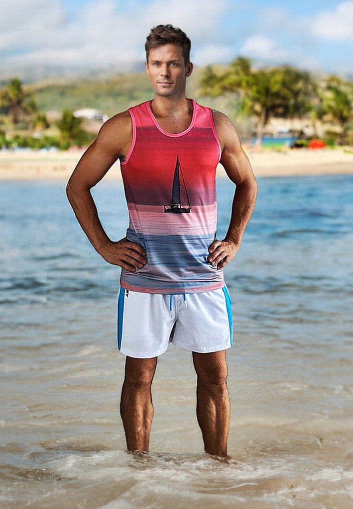 young man wearing sleeveless red and pink gradient tank top with sailboat design and white shorts standing in shallow ocean water on tropical beach