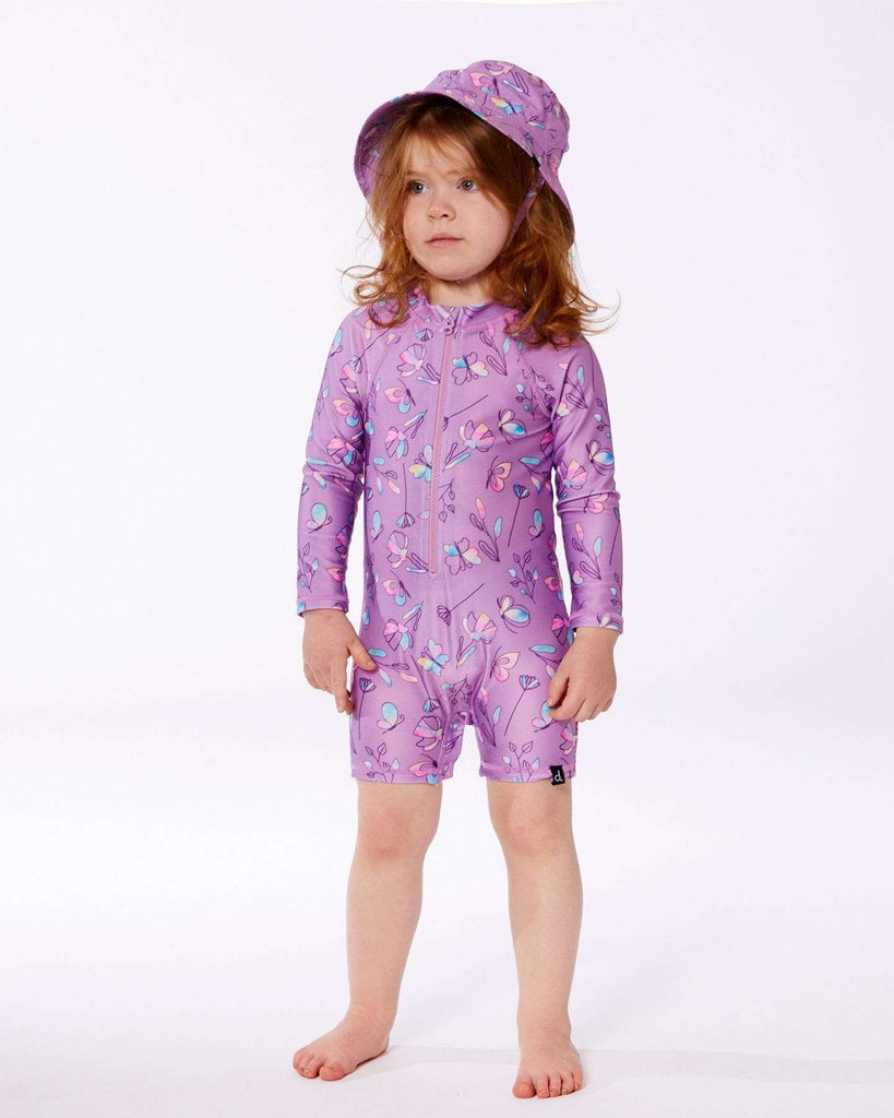 child wearing purple floral long-sleeve romper with matching hat against white background