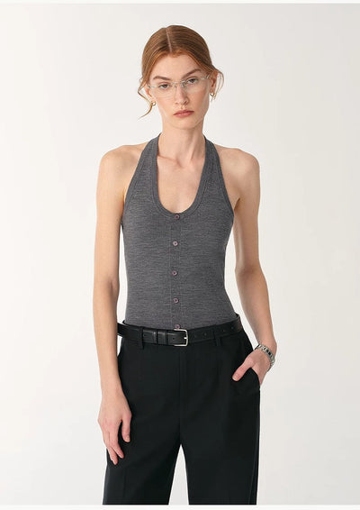 Woman wearing fitted grey German Yangzi 48S machine washable wool halter neck jumpsuit with button details and black pants