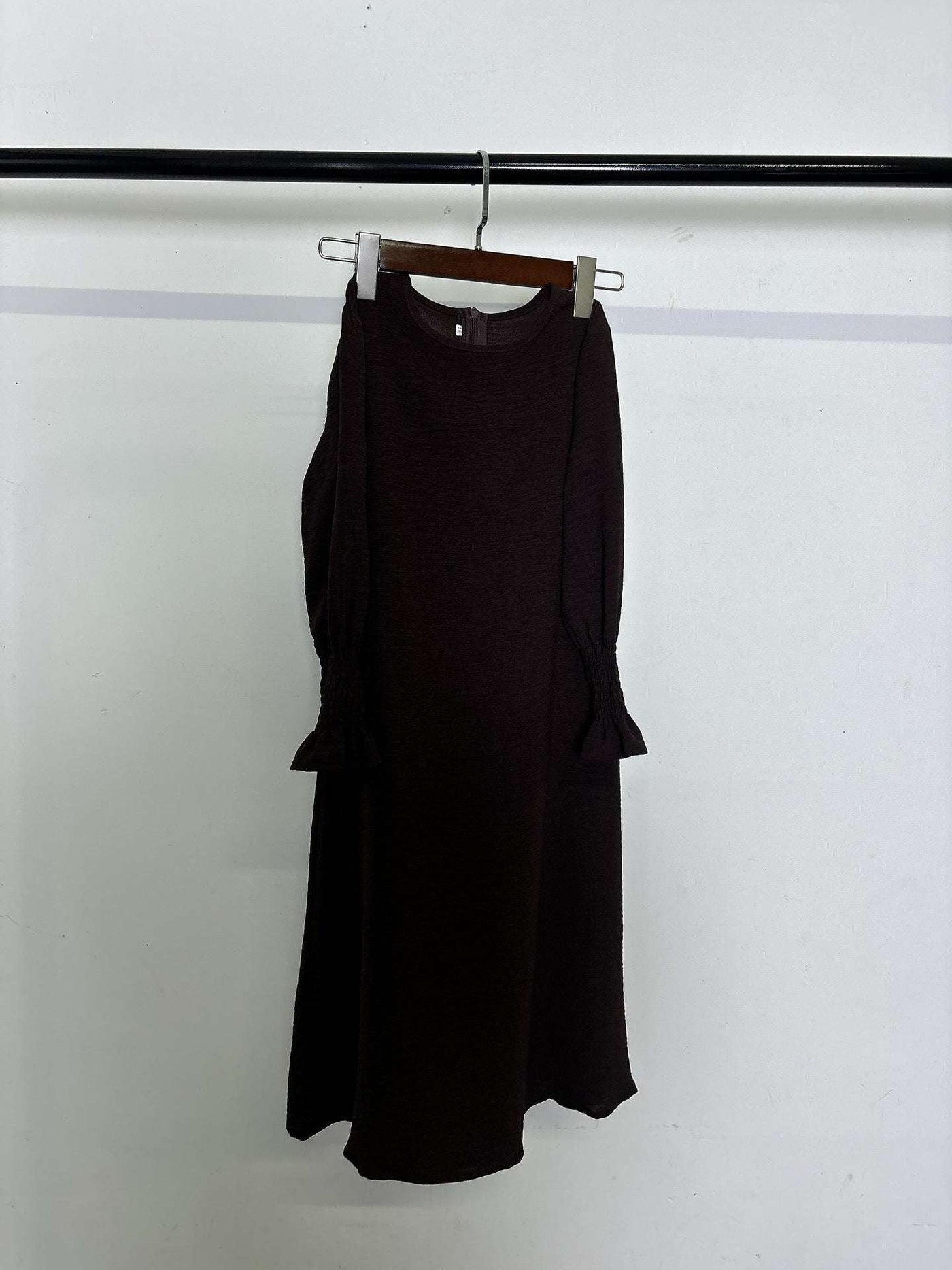 Long black polyester dress with round neck and wavy ruffled long sleeves hanging on wooden hanger
