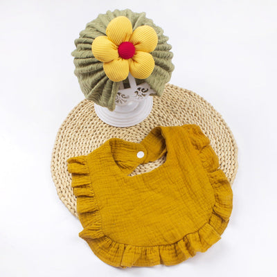 Newborn baby hat and bib set with frilly trim made of soft organic cotton muslin, featuring a green bonnet with a yellow flower and a mustard yellow drool bib