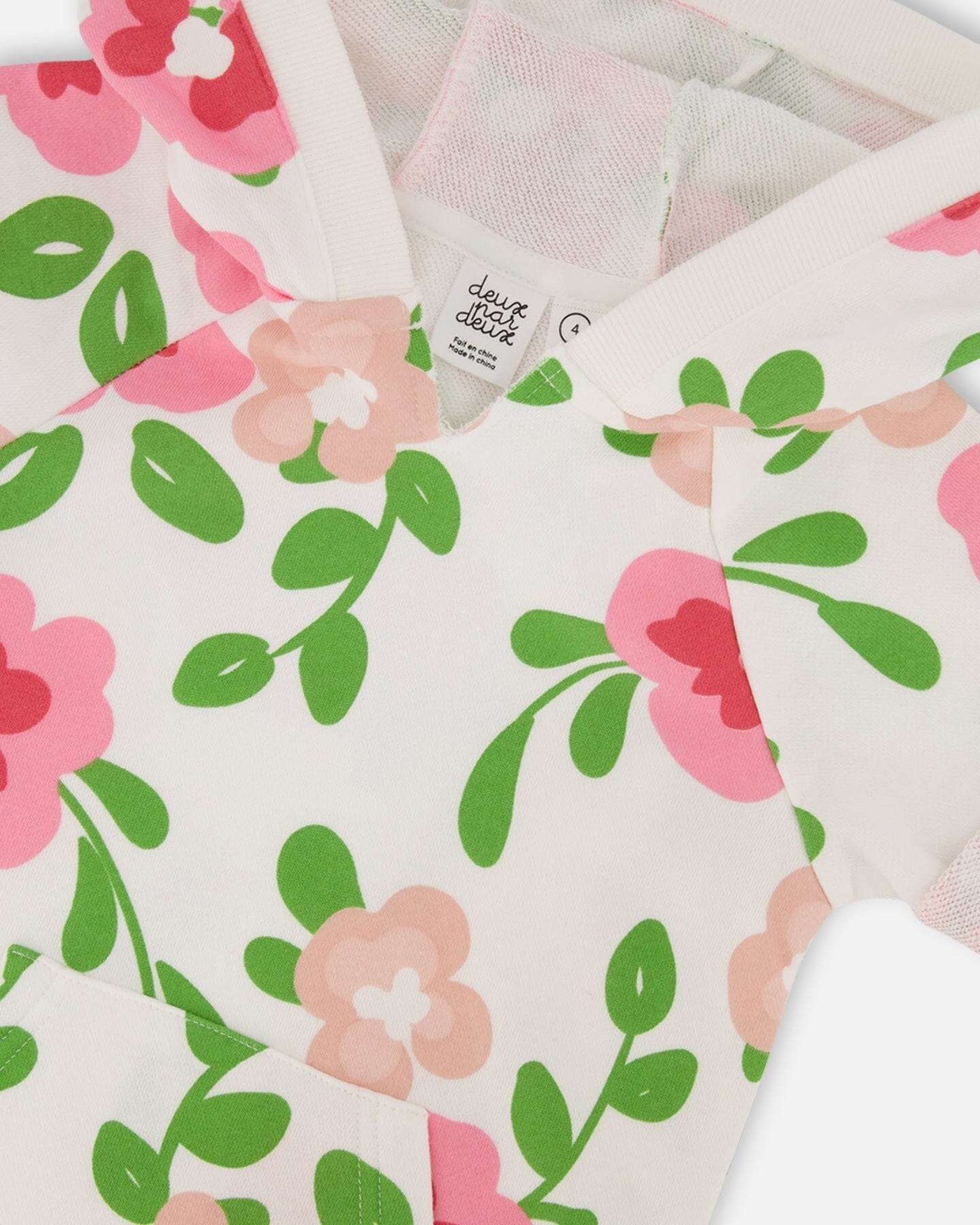 Close-up of printed French terry fabric with pink flowers and green leaves on white background from hooded dress