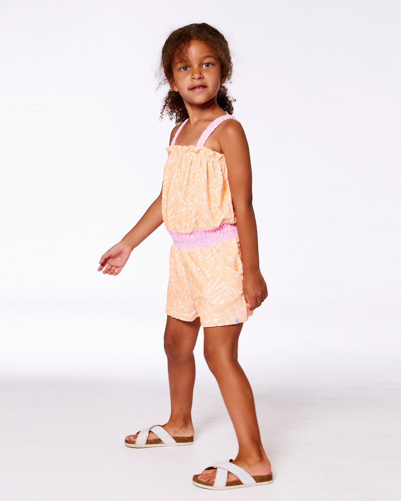 Girl wearing vibrant orange and white printed terry cloth romper with flat straps and elastic waistband