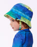 Little boy wearing blue dinosaur-patterned sun hat and matching swim shirt facing left on white background
