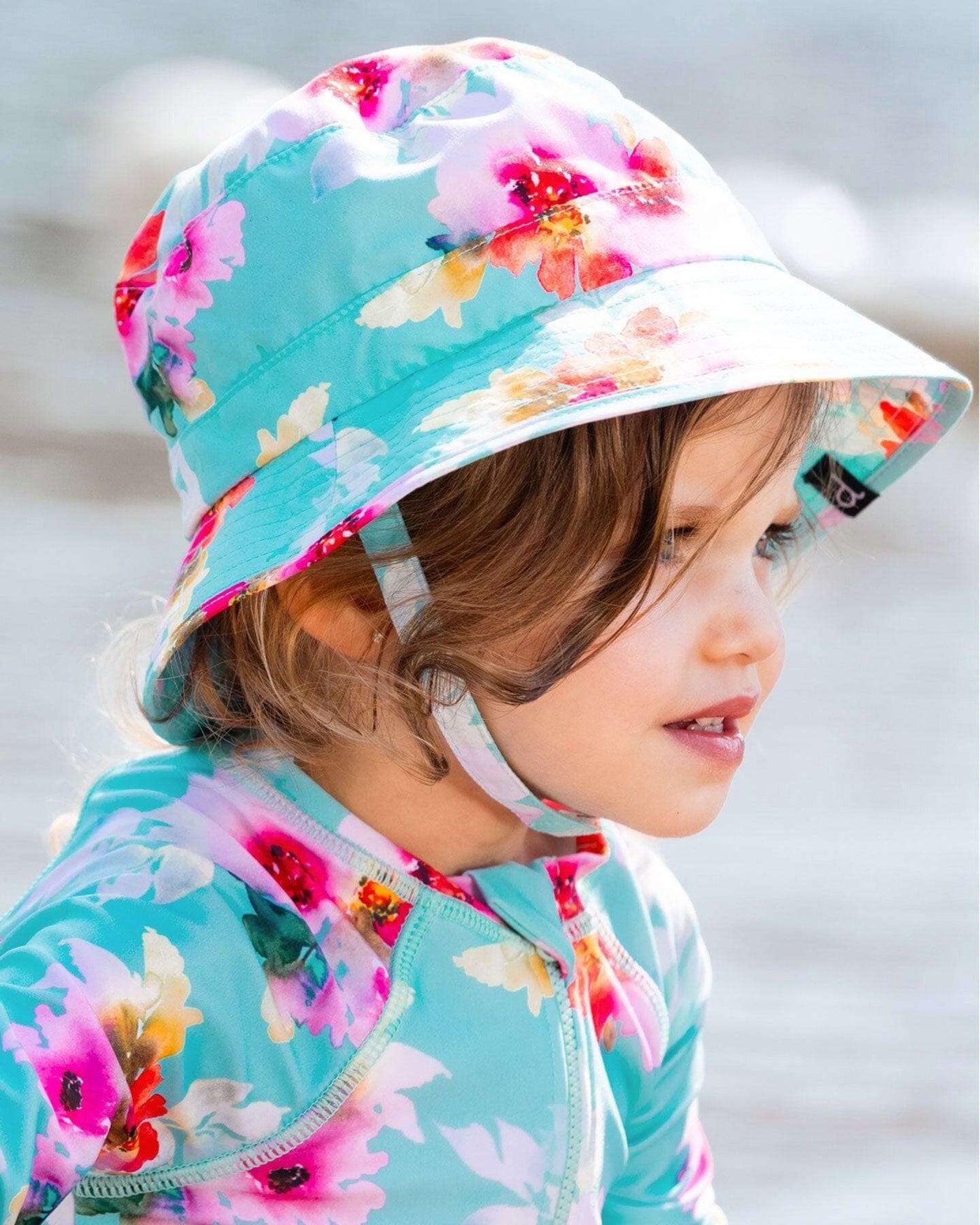 Child wearing a turquoise bucket hat with pink and white floral print and chin strap for sun protection