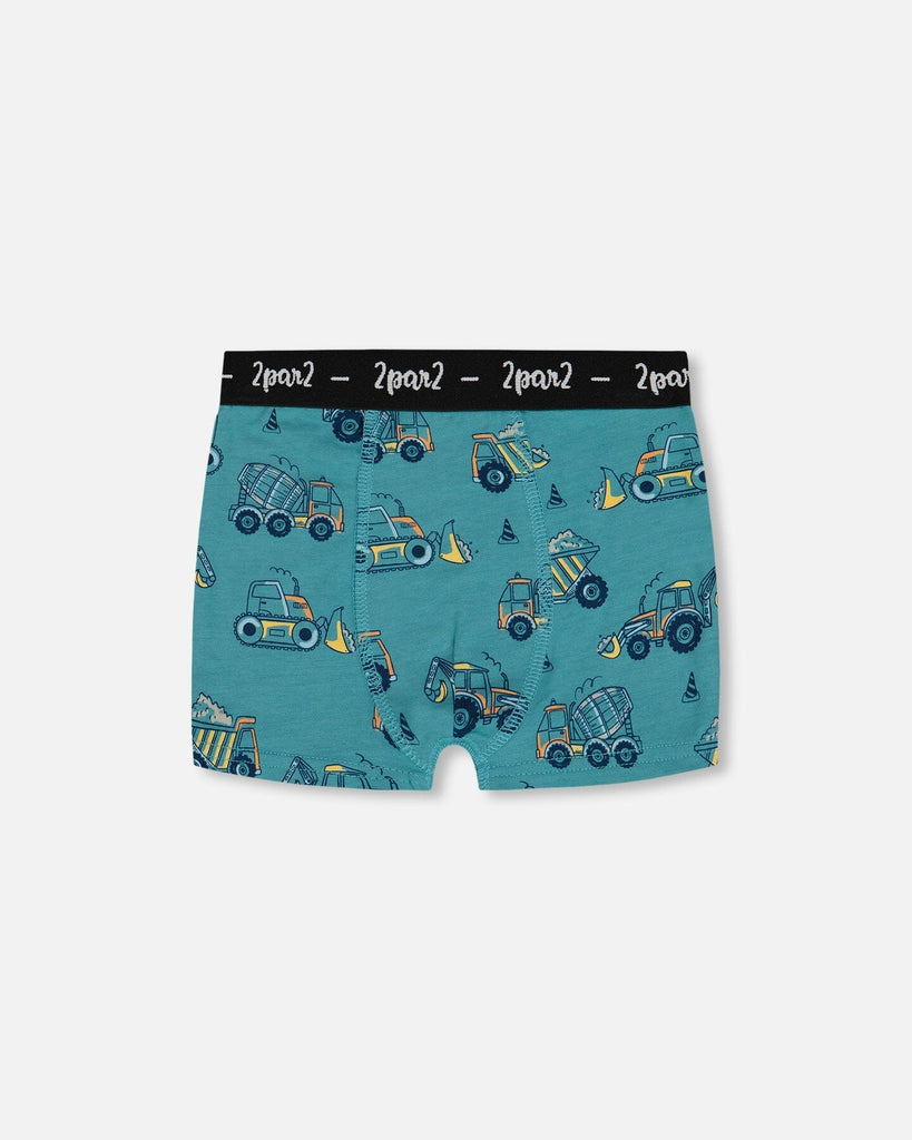 Printed organic cotton boxer shorts in teal with yellow truck pattern and black elastic waistband.