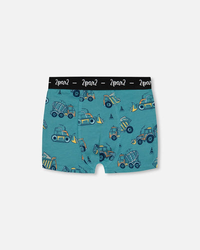 Printed organic cotton boxer shorts in teal with yellow truck pattern and black elastic waistband.