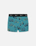 Printed organic cotton boxer shorts in teal with yellow truck pattern and black elastic waistband.