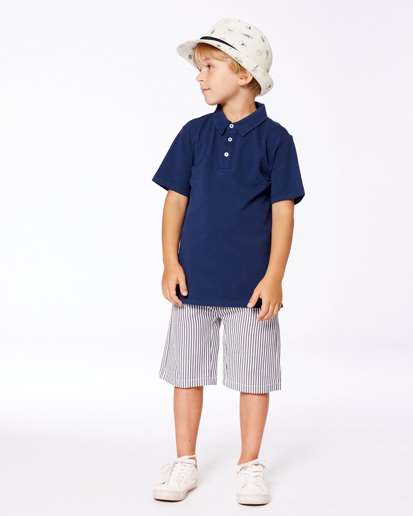 Boy wearing navy blue short sleeve polo shirt with striped shorts and white sneakers