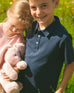 Boy wearing navy blue short sleeve polo shirt standing outdoors with girl holding pink stuffed bunny