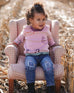 Toddler wearing jeans blue denim with embroidered details sitting on pink checkered armchair outdoors