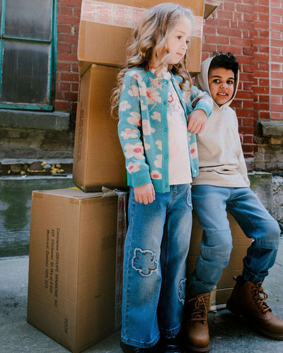 Kids wearing wide leg stretch light blue denim jeans with flower stitching outdoors by cardboard boxes