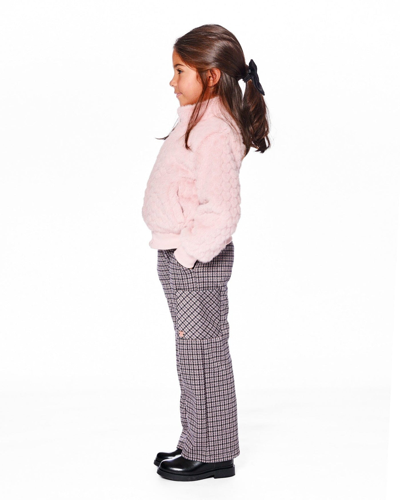 Girl wearing jacquard knit flare pants with houndstooth pattern and cargo pockets paired with a pink fuzzy sweater and black shoes.