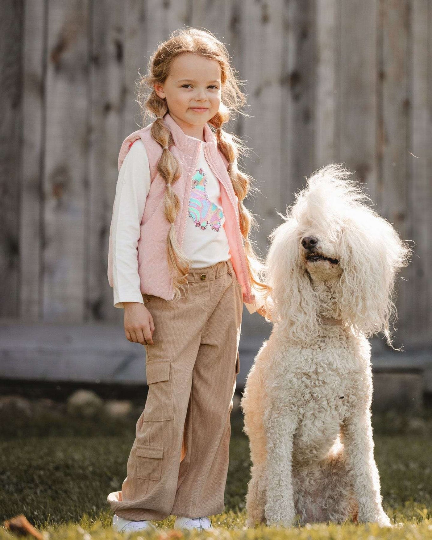 Young girl wearing light pecan brown parachute corduroy pants with cargo pockets standing next to a large fluffy white dog outdoors