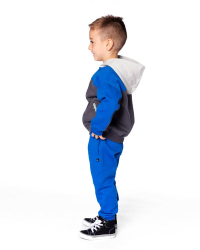 Young boy wearing blue fleece sweatpants with side pockets and drawstring waistband, paired with a hooded sweatshirt and black sneakers.