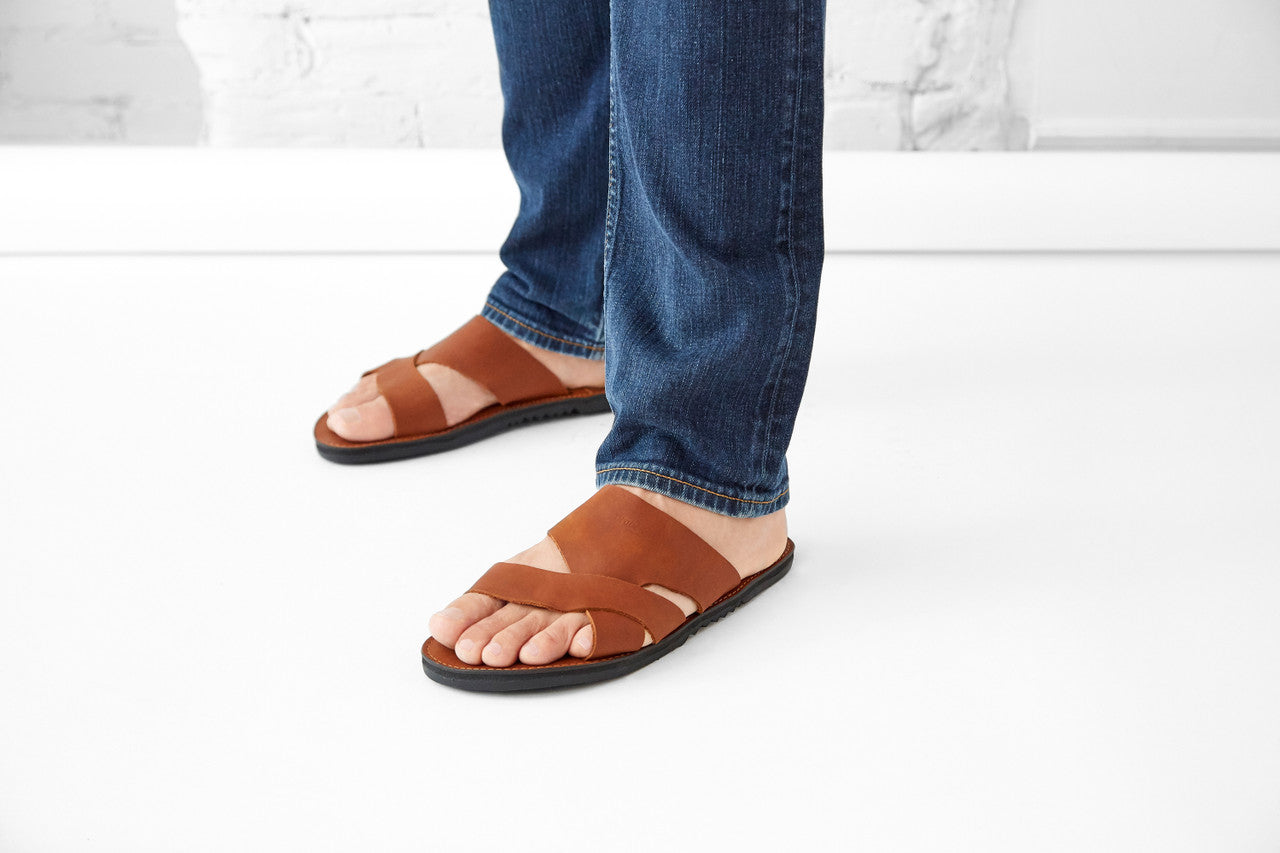 The Mateo Men's Leather Slide sandal in brown leather with arch support and handcrafted sole shown on feet with jeans