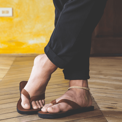 The Novio men's leather flip flops with handcrafted leather uppers and cushioned foam sole on wooden floor background