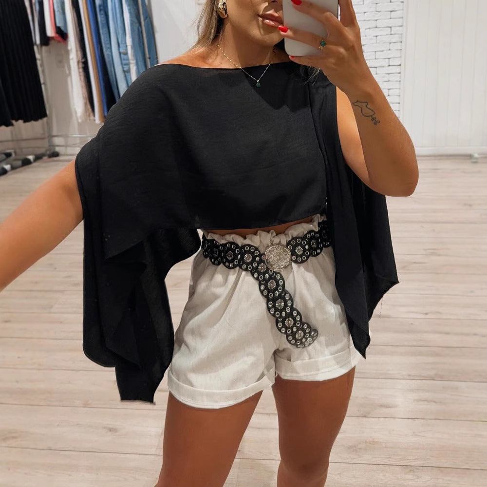 Woman wearing black off-shoulder bell sleeve top with white shorts and decorative belt in a boutique setting