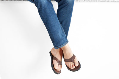The Padre men's brown leather flip flop with cushioned sole worn with blue jeans sitting on white background
