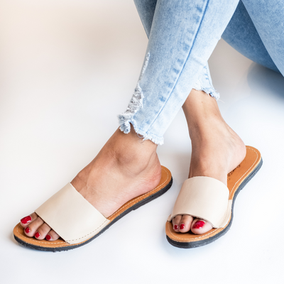The Linda leather slide sandal in beige with cushioned sole and ankle strap worn with frayed light blue jeans