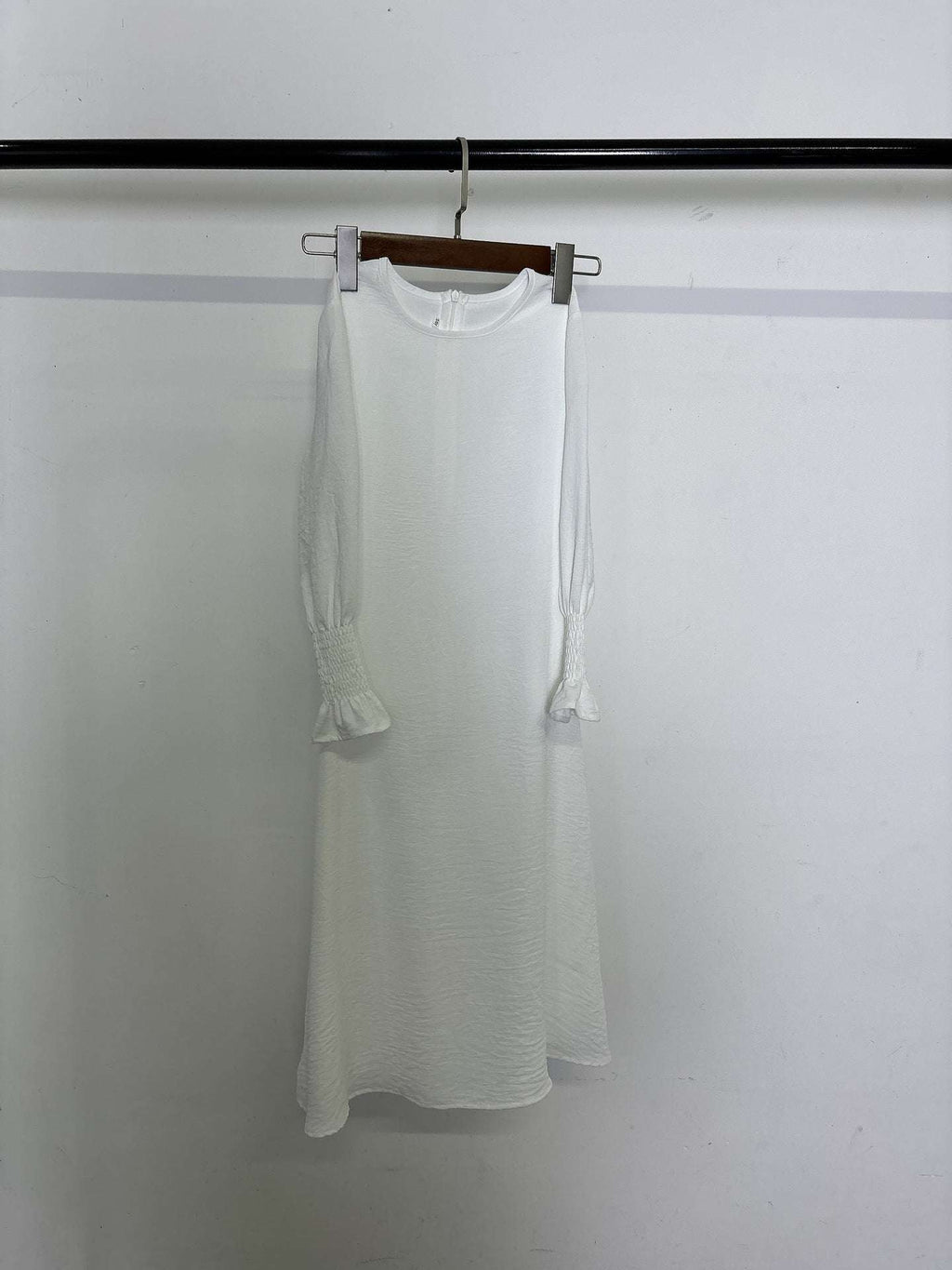 White round neck long sleeve dress with wavy ruffled cuffs and pleated polyester fabric hanging on wooden hanger