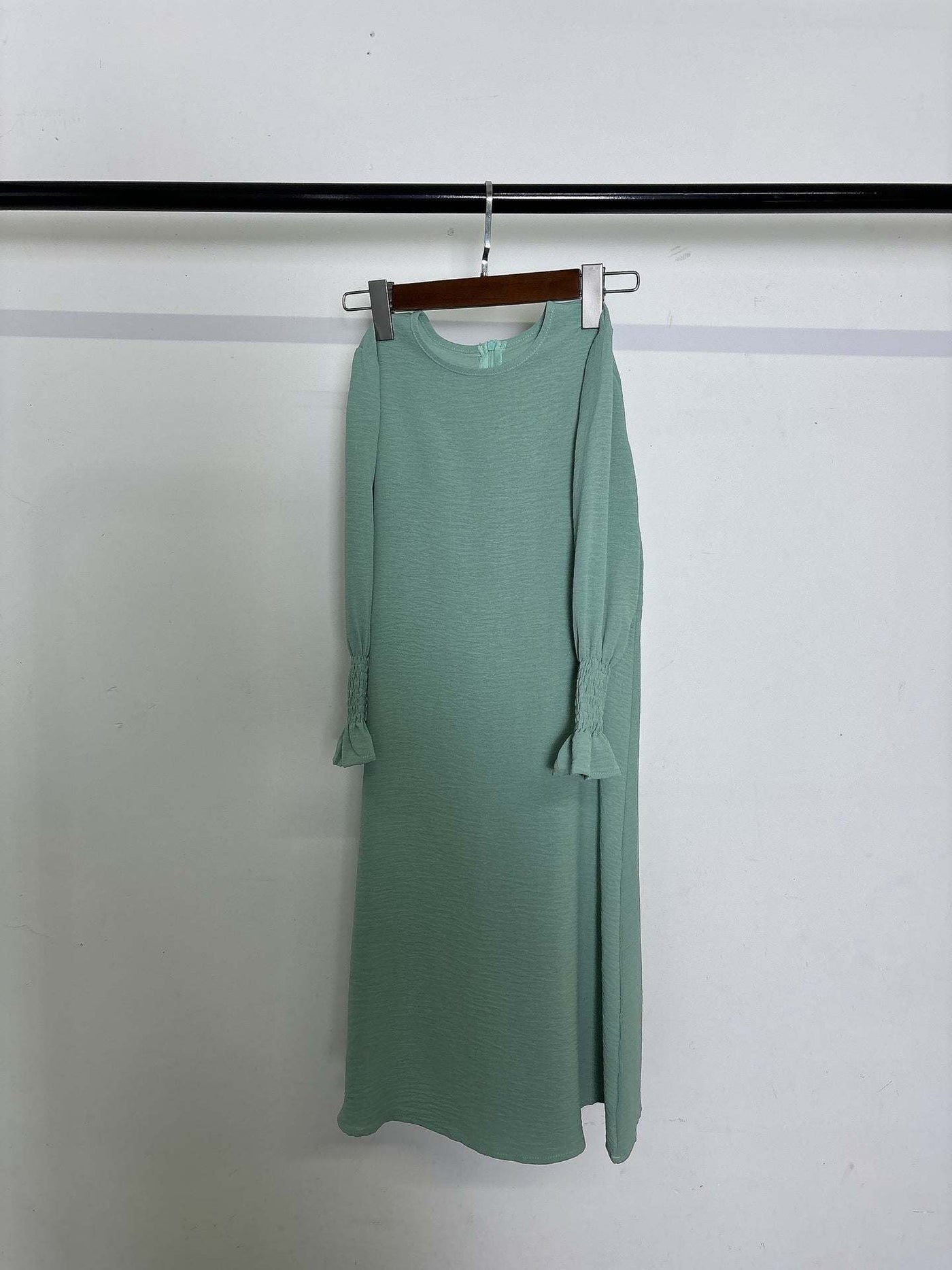 Round neck wavy ruffled solid color long sleeve dress in green polyester fabric hanging on a rack