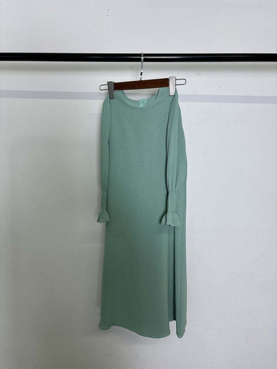 Round neck wavy ruffled solid color long sleeve dress in green polyester fabric hanging on a rack