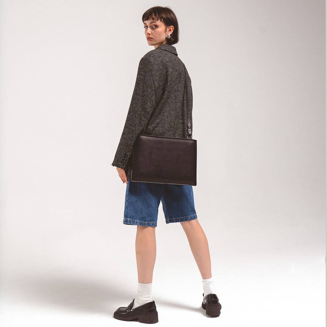 Woman wearing black slim leather sleeve for iPad with adjustable shoulder strap and casual outfit
