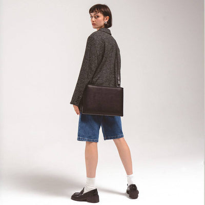 Woman wearing black slim leather sleeve for iPad with adjustable shoulder strap and casual outfit