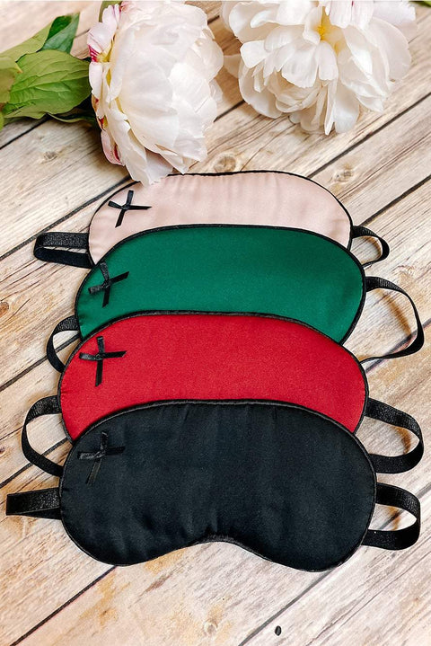Set of satin sleep masks in multiple colors with small bows and adjustable straps on wooden surface with white flowers